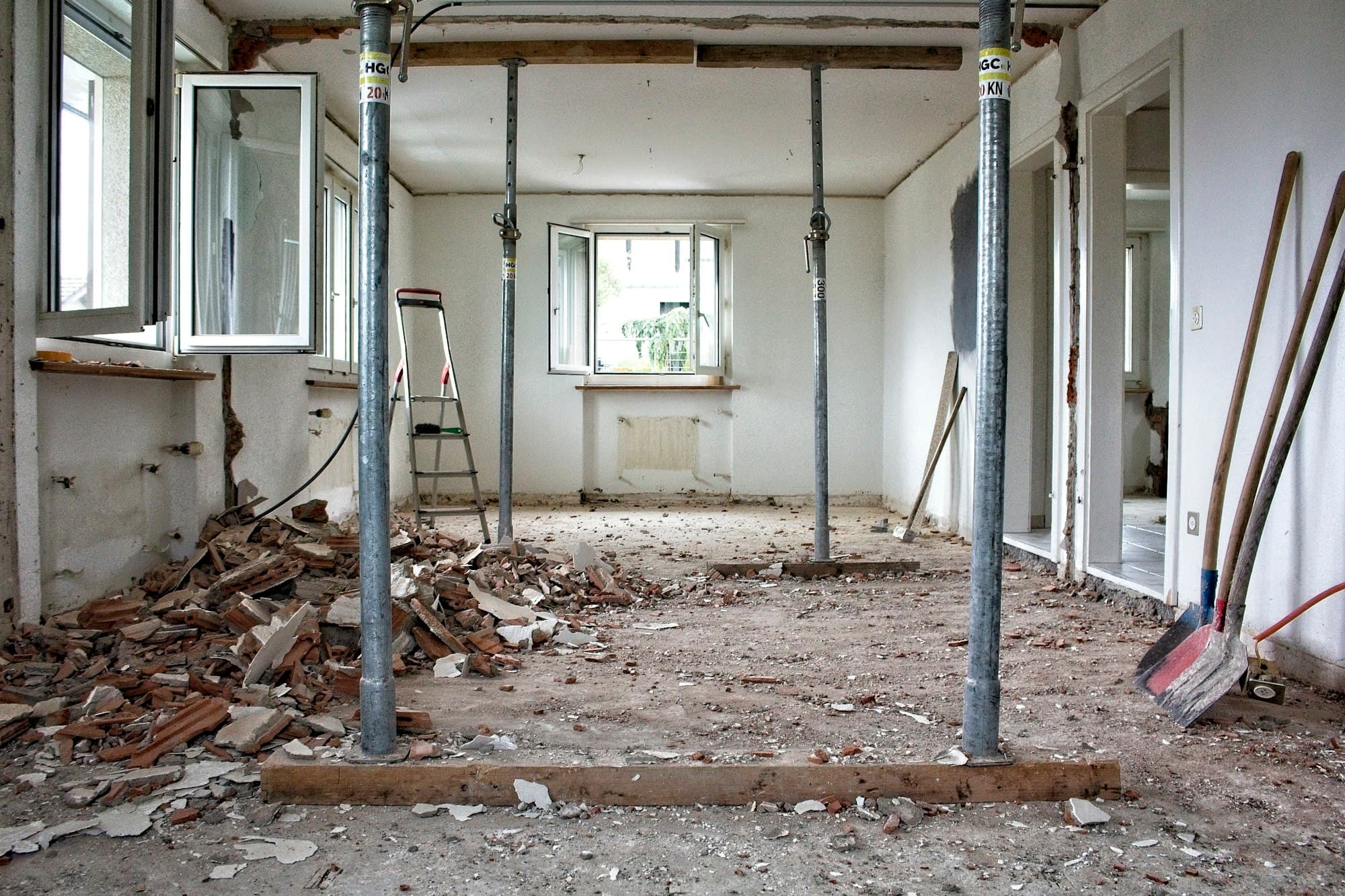 A gutted room in the middle of a remodel, with temporary support posts, rubble and tools on the floor