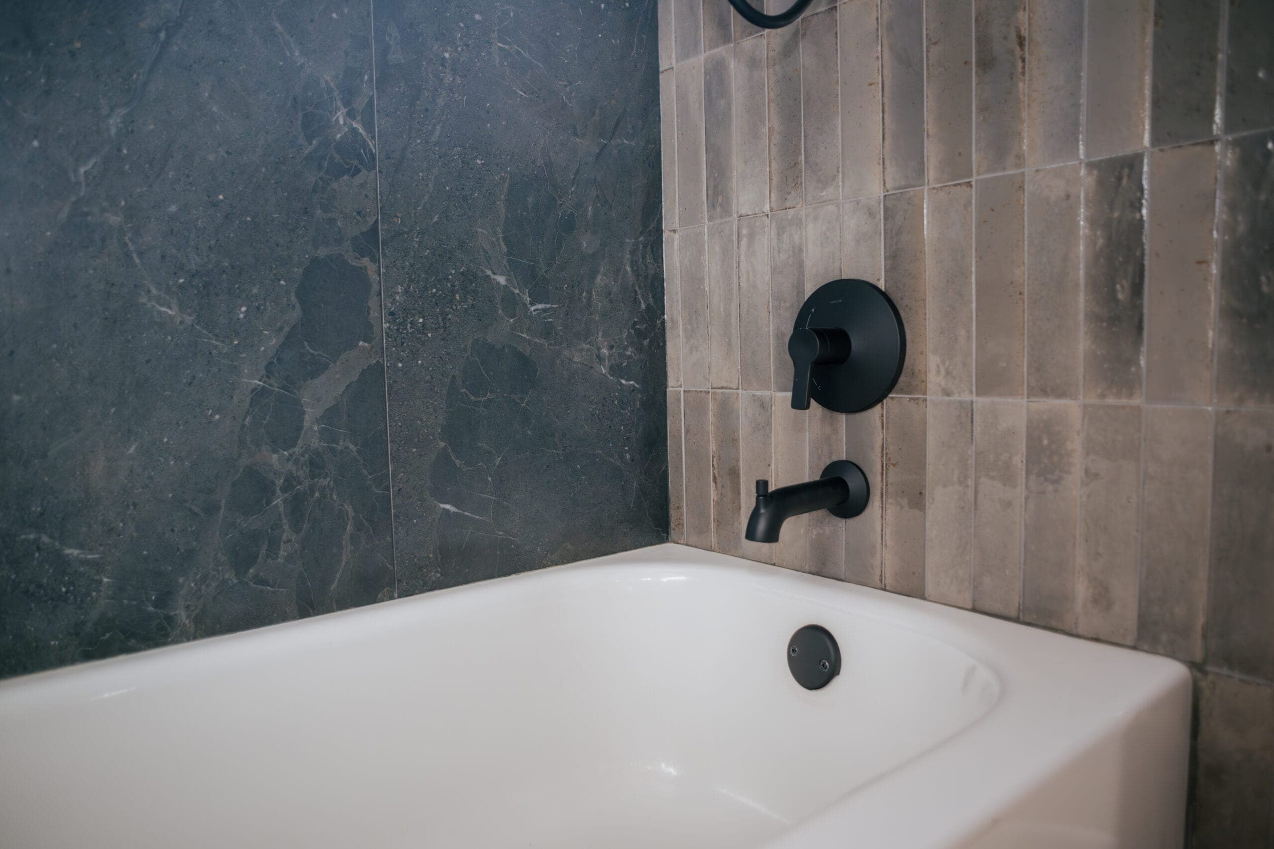 White alcove tub with matte black tub filler and valve against dark tile