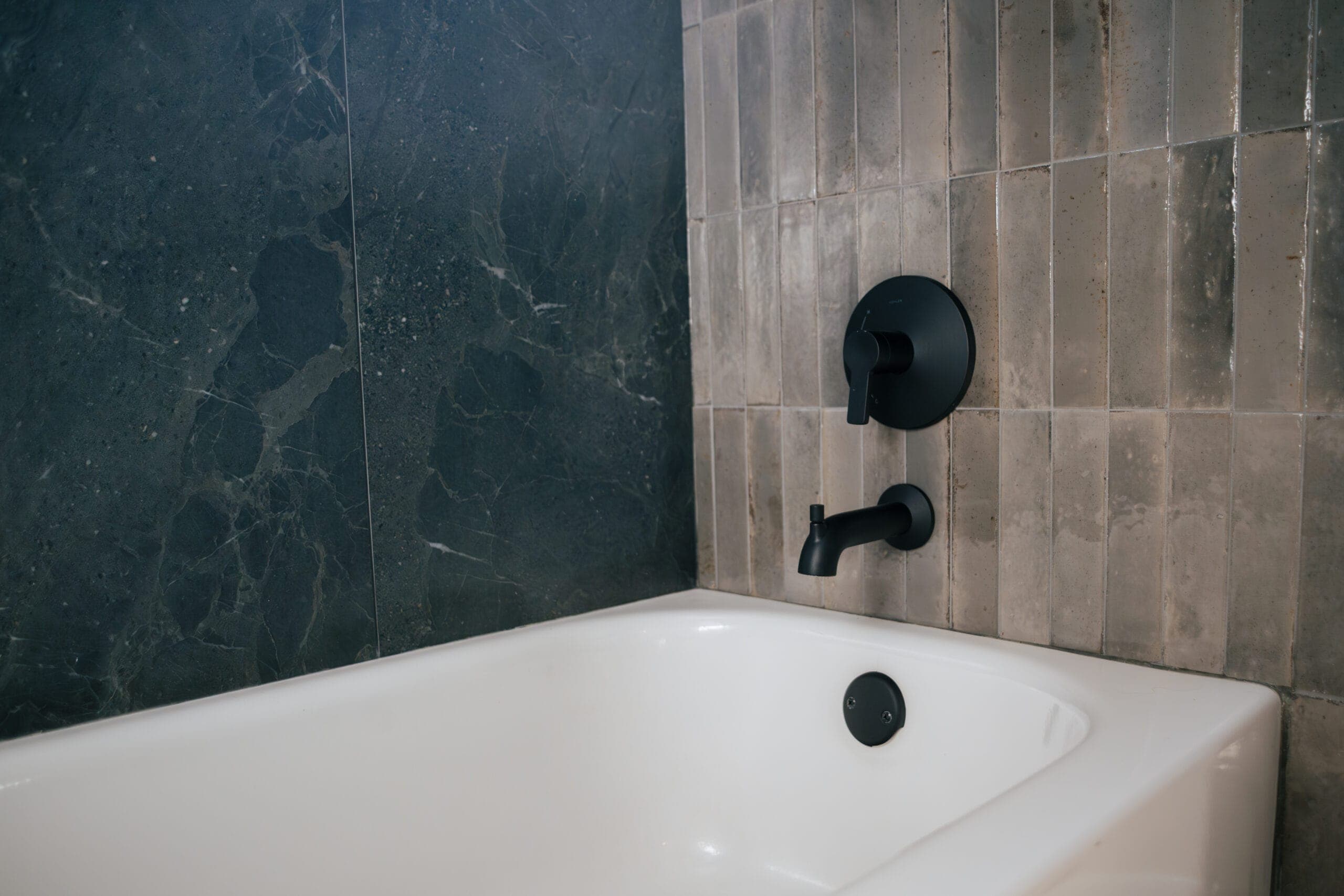 Tub surround in mixed dark and warm-toned tile in a small bathroom remodel