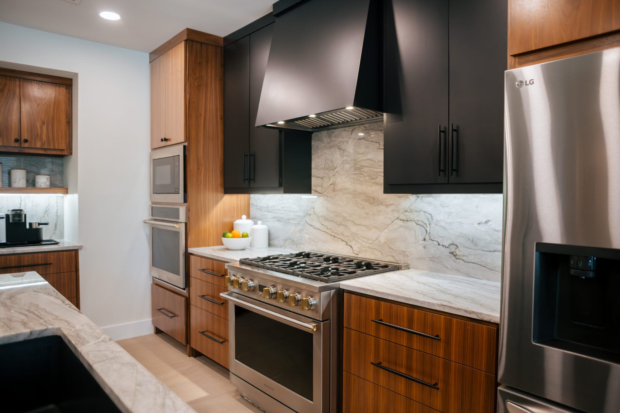 Walnut and matte black flat-panel cabinets with a black range hood and full-height stone backsplash — kitchen remodeling by Southlake Luxury Kitchens, serving Southlake, TX