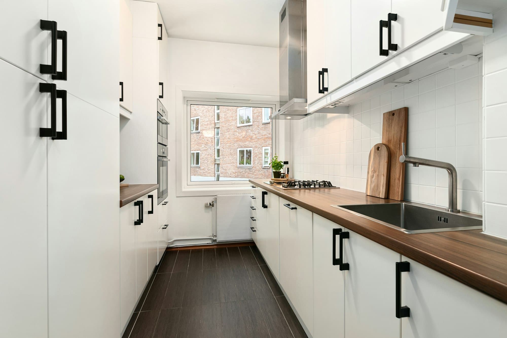 Galley kitchen with white flat-panel cabinets on both sides, wood countertops and a window at the far end