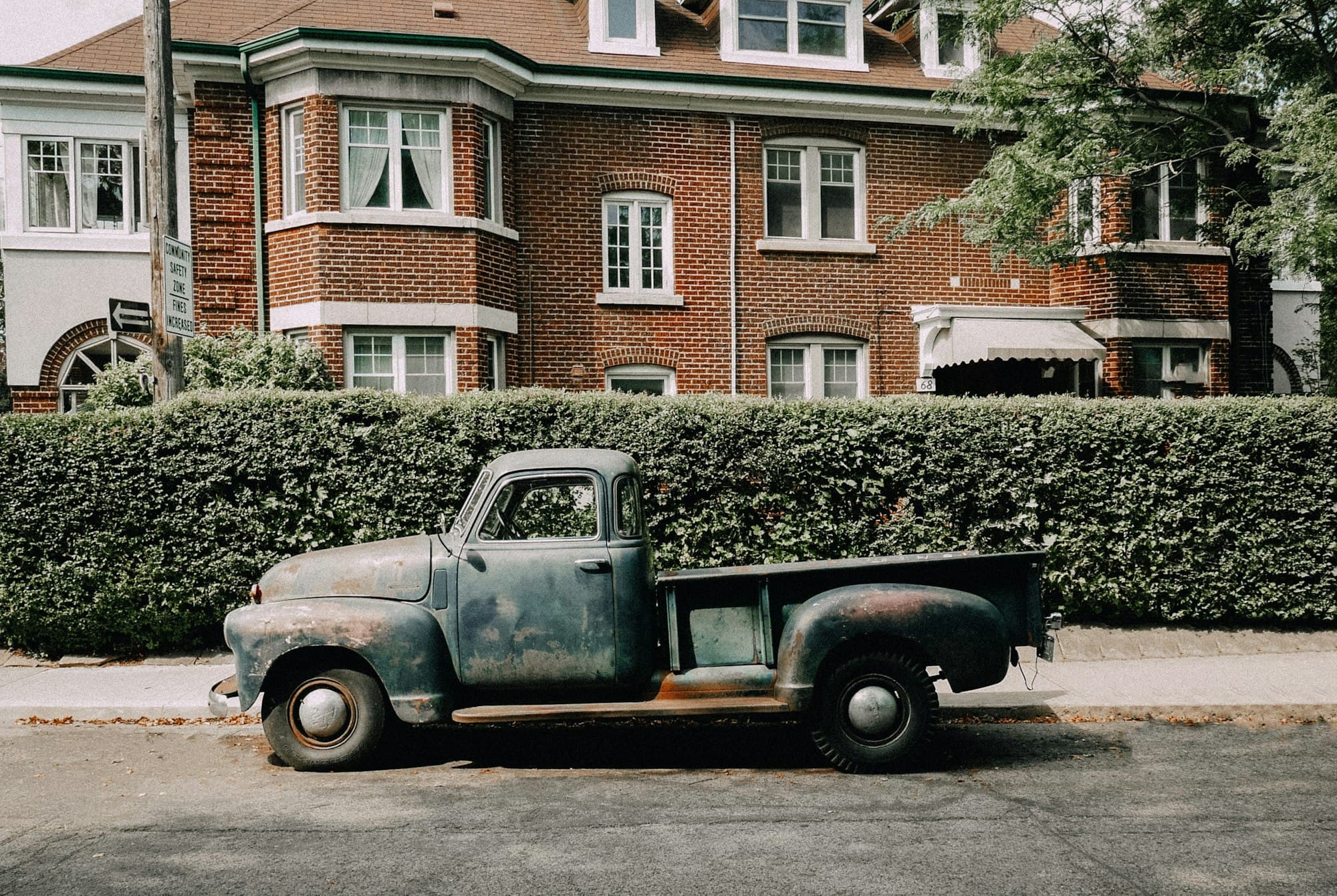 Old weathered pickup truck parked on the street outside a brick house