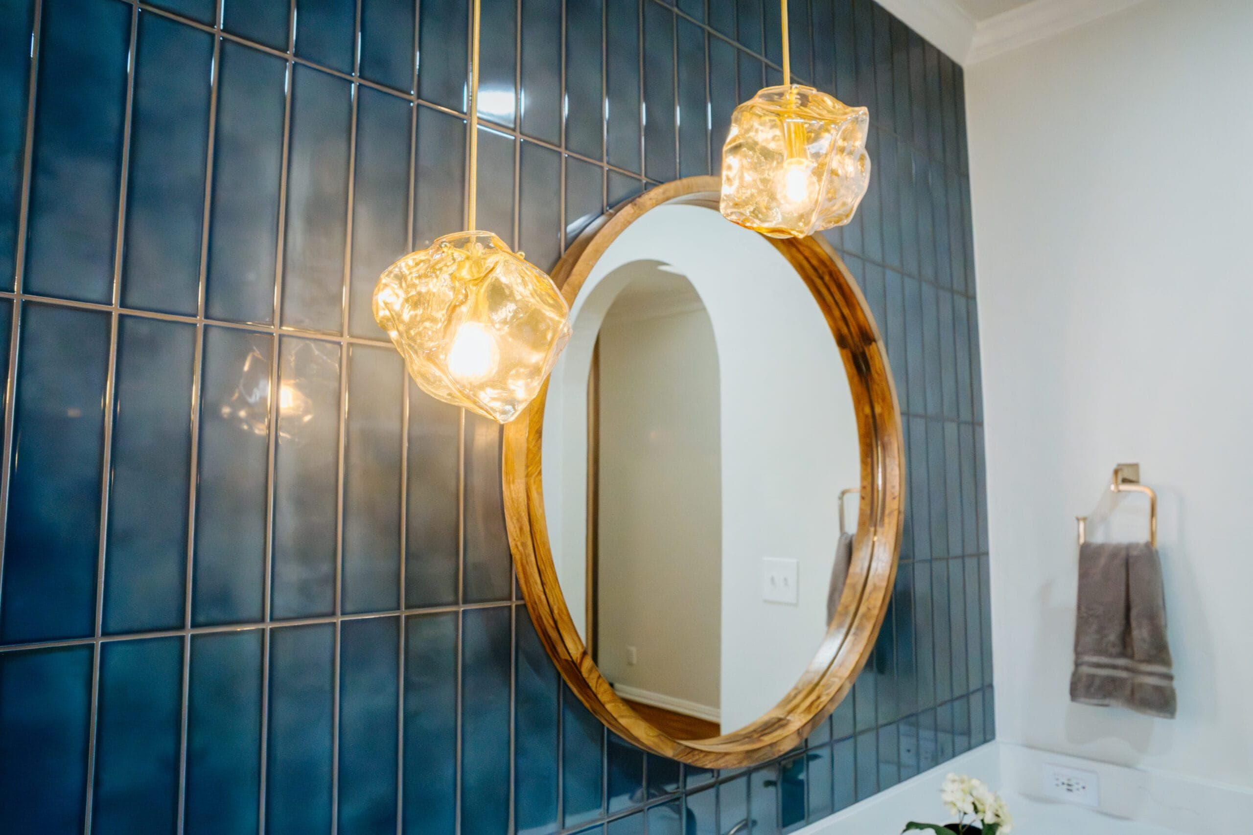 Glass globe pendants flanking a wood-framed oval mirror on blue tile