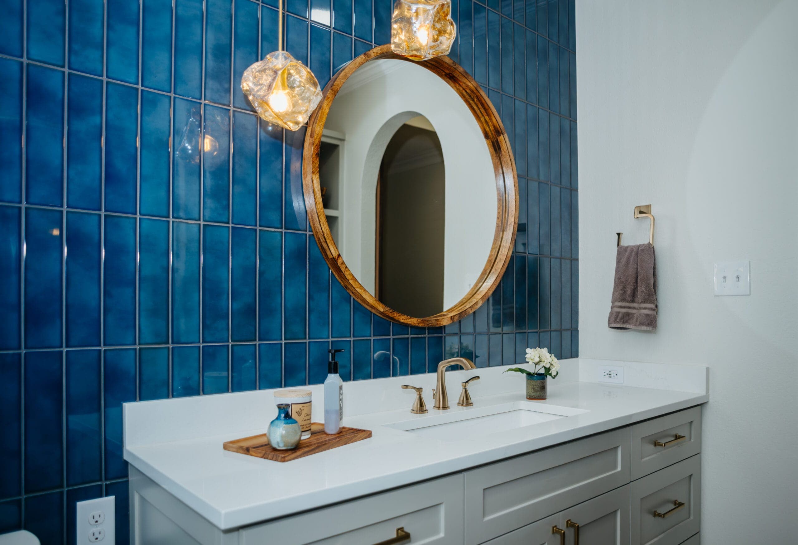 Glossy blue stacked tile wall with a wood-framed oval mirror and glass globe pendants — bathroom remodeling by Southlake Luxury Kitchens, serving Southlake, TX