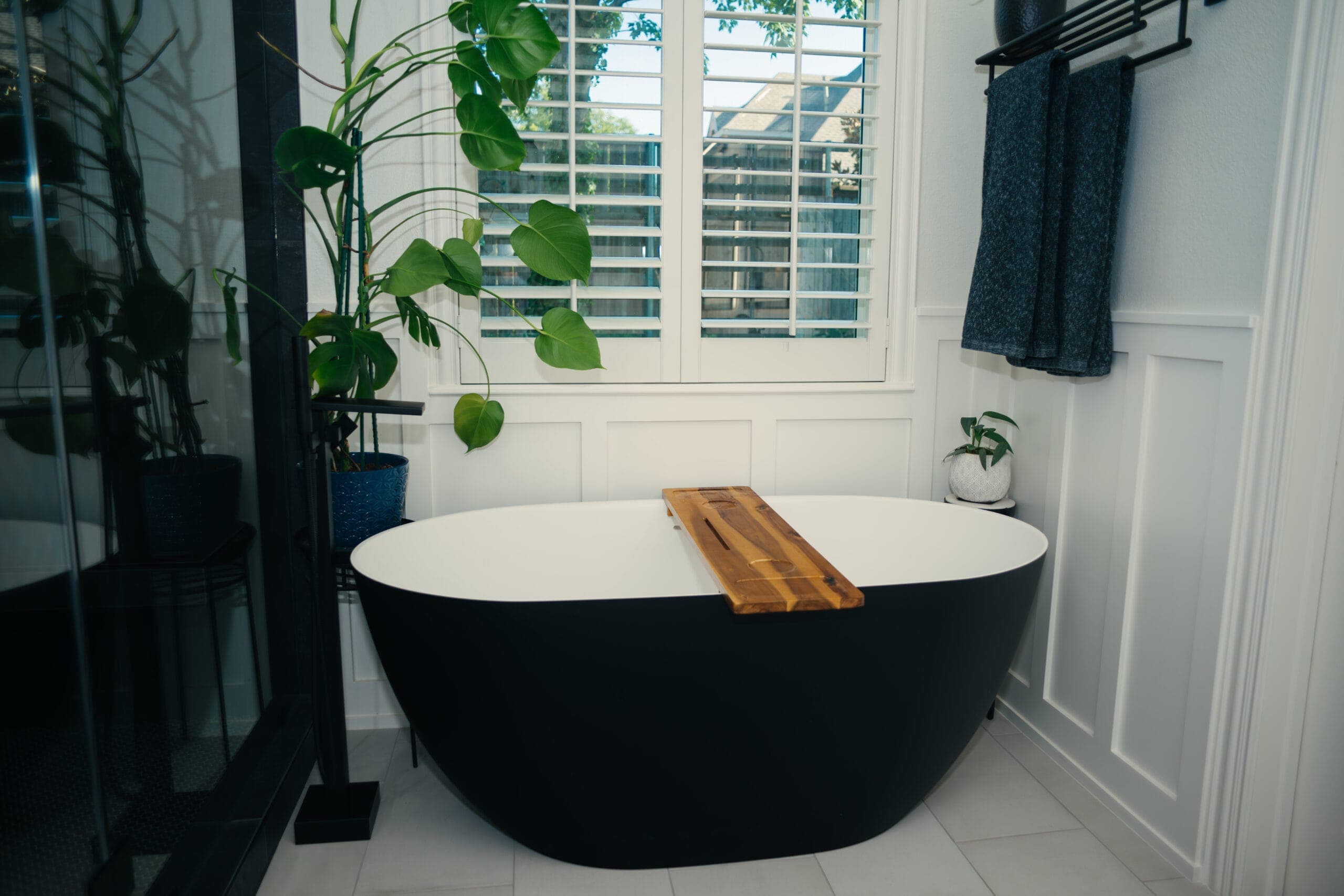 Freestanding soaking tub in front of plantation shutters and wainscot paneling