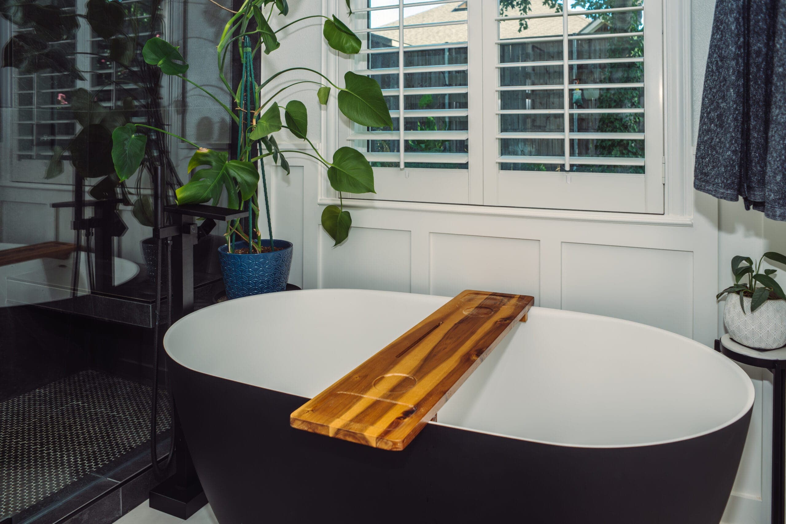Black soaking tub with a wood bath caddy and greenery alongside