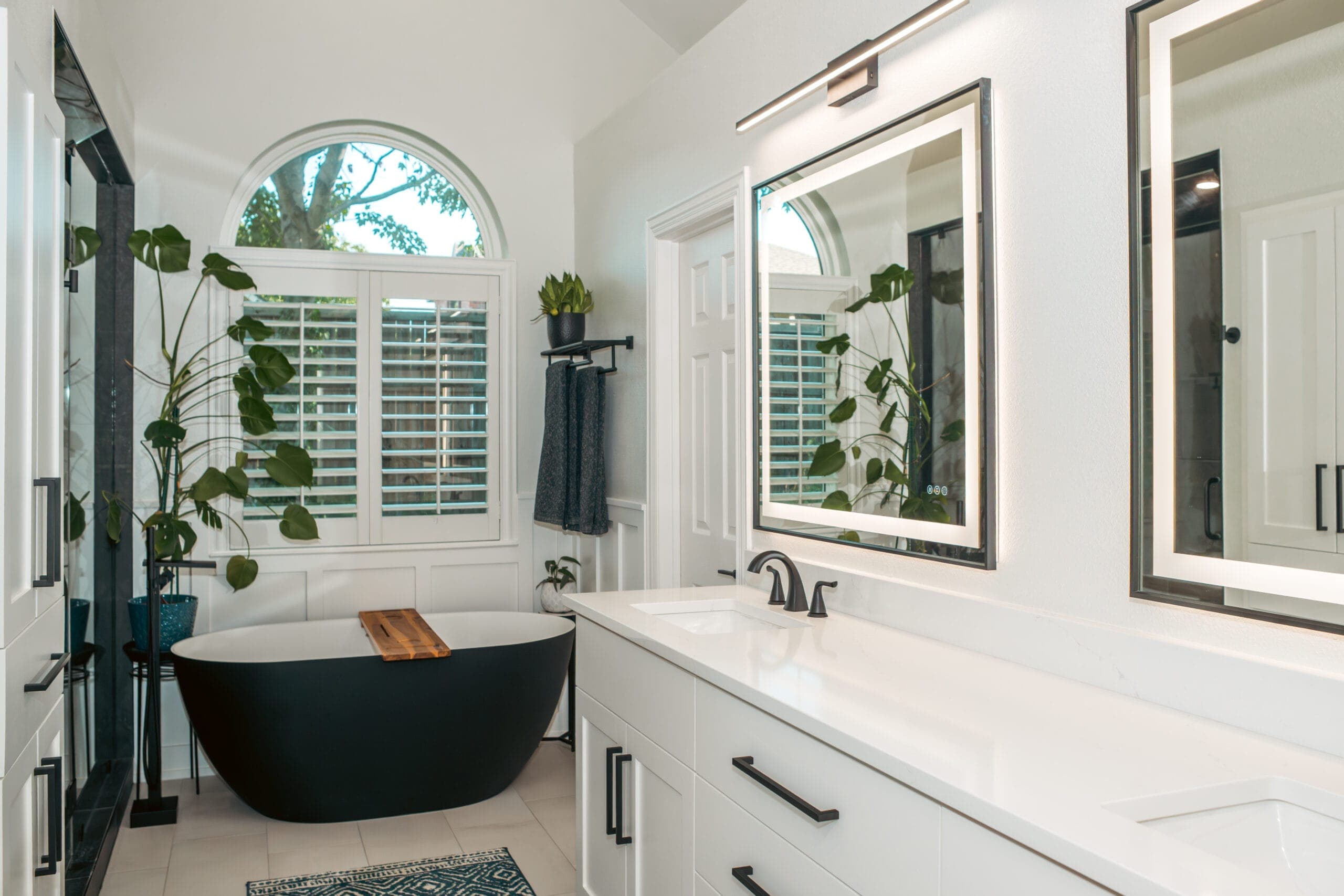 Black freestanding tub beneath an arched window in a white paneled bathroom — bathroom remodeling by Southlake Luxury Kitchens, serving Southlake, TX