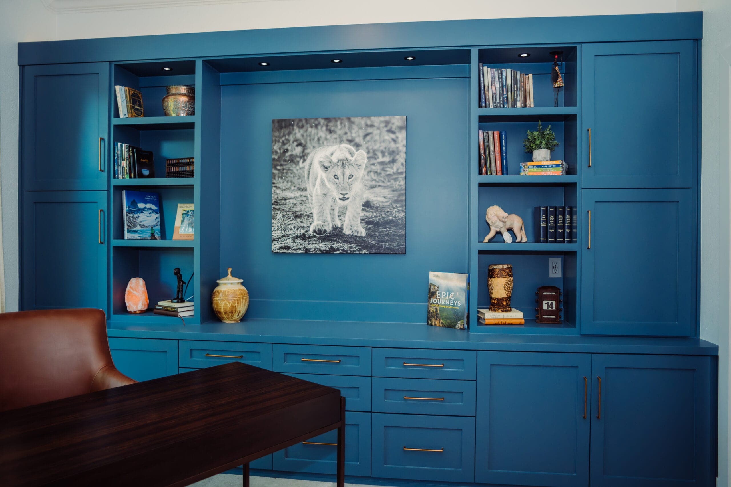 Blue built-in cabinetry framing a dark wood desk and leather chair