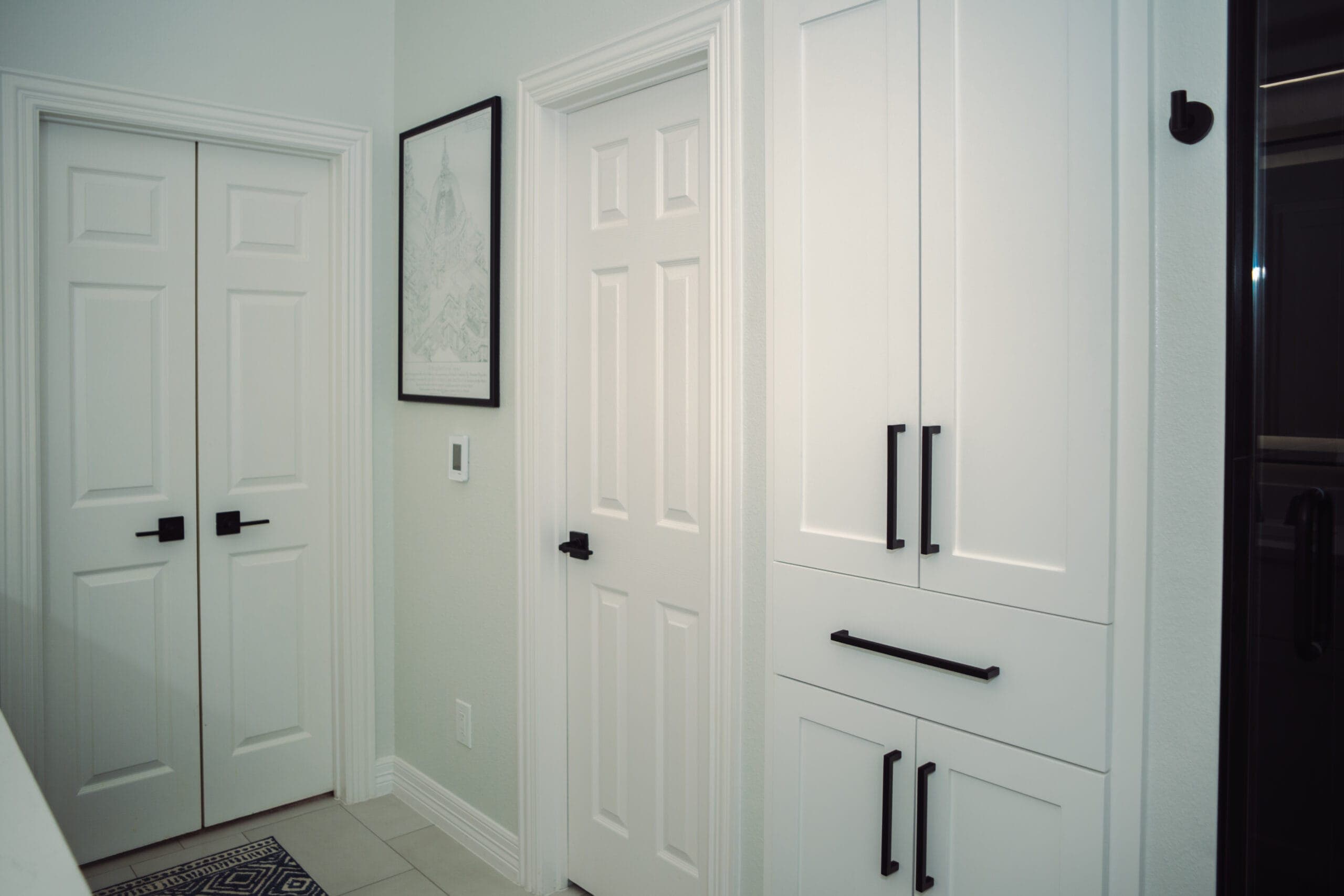 Built-in linen cabinet with matte black bar pulls beside the vanity