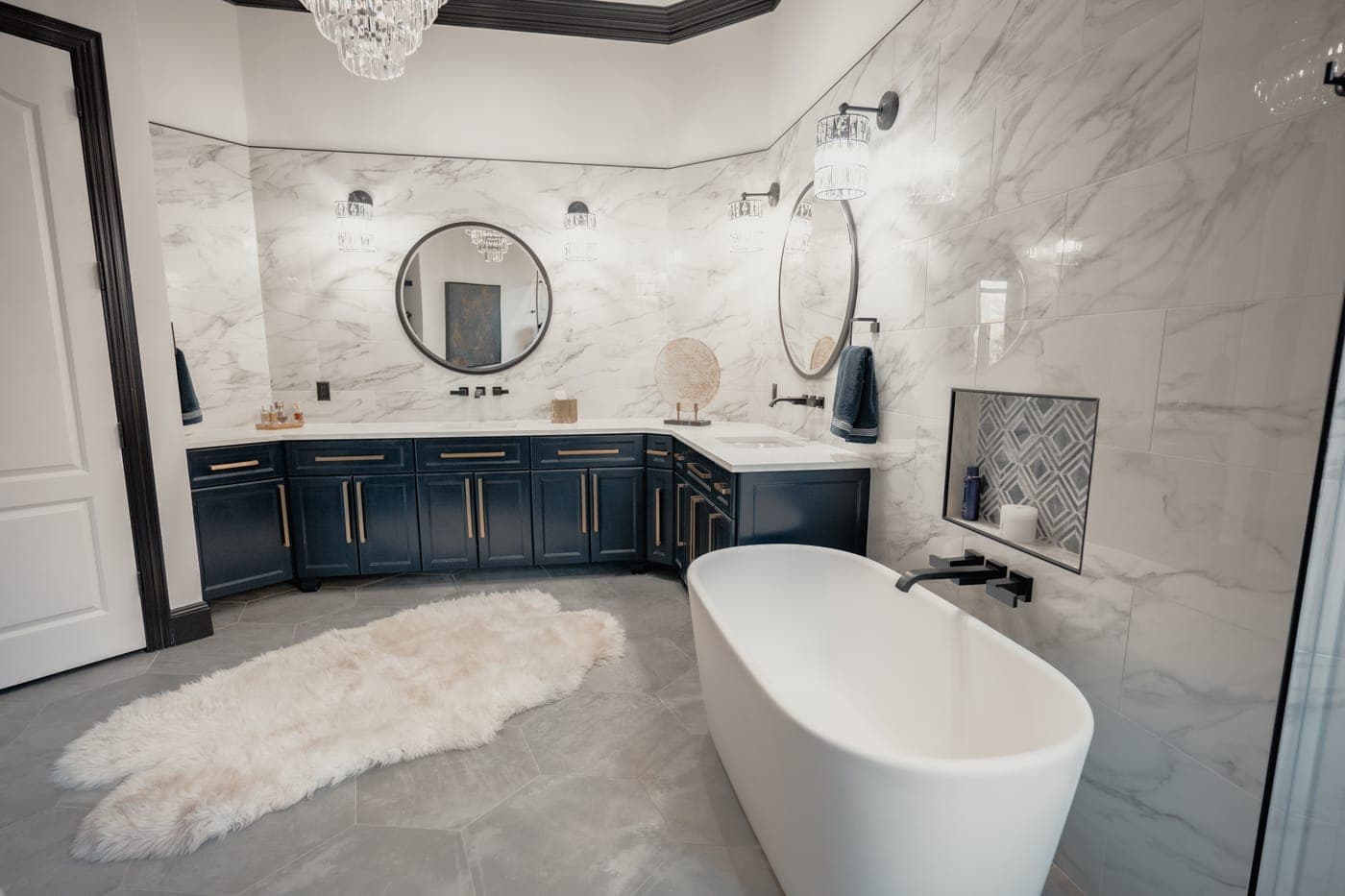 Freestanding tub beneath a crystal chandelier with a sheepskin rug alongside