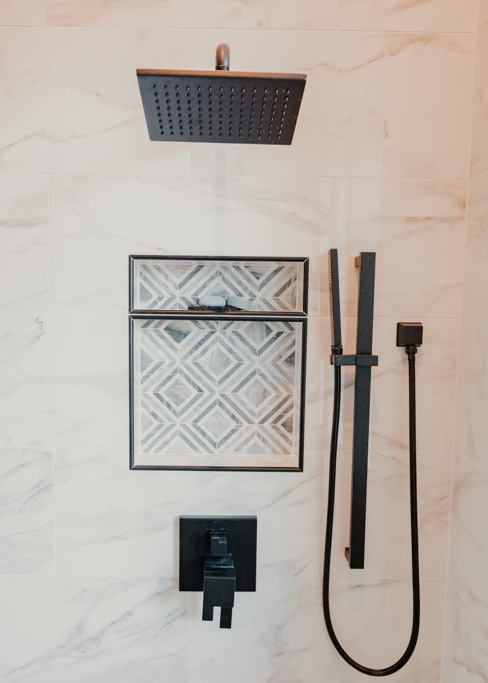 Square rainfall shower head and matte black shower fixtures on marble-look tile