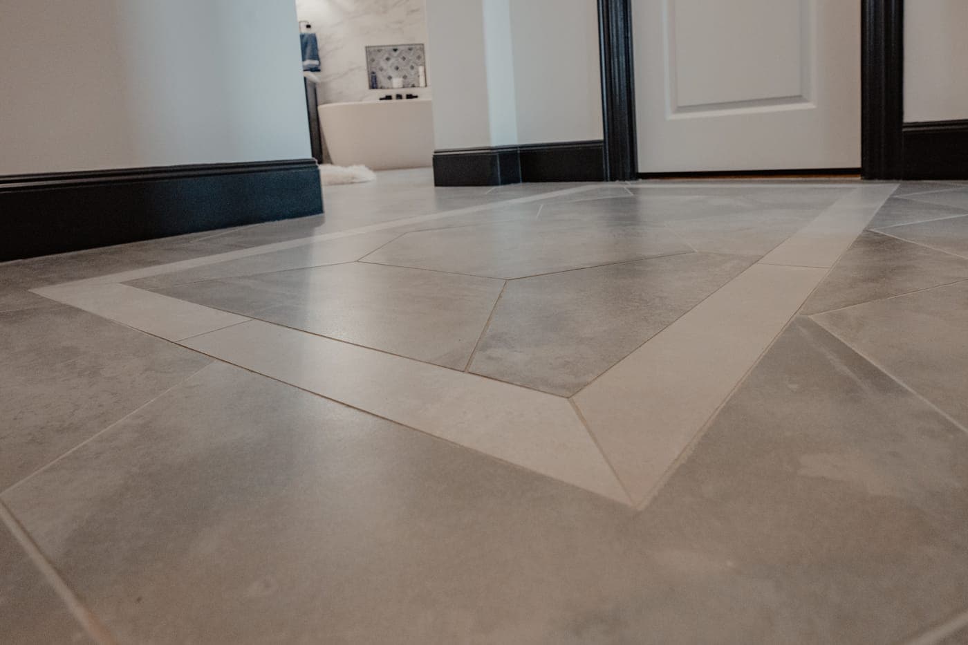 Large-format floor tile with a mitered border inlay at the bathroom entry