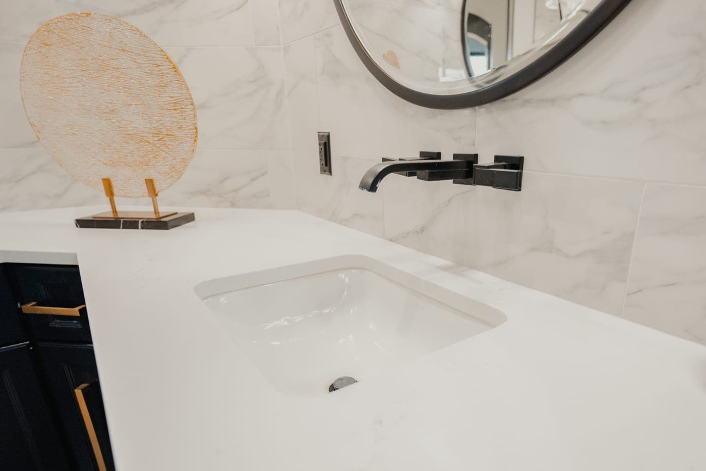 Undermount sink with a matte black wall-mounted faucet on a white quartz counter