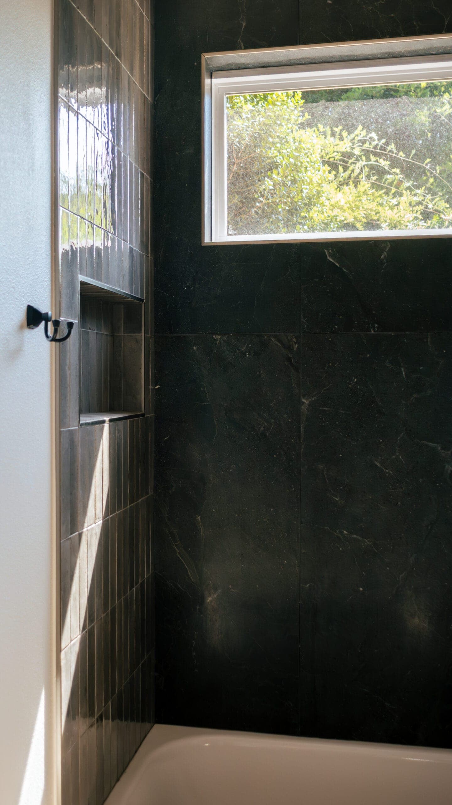 Small bathroom shower finished in dark large-format tile with a window above the tub