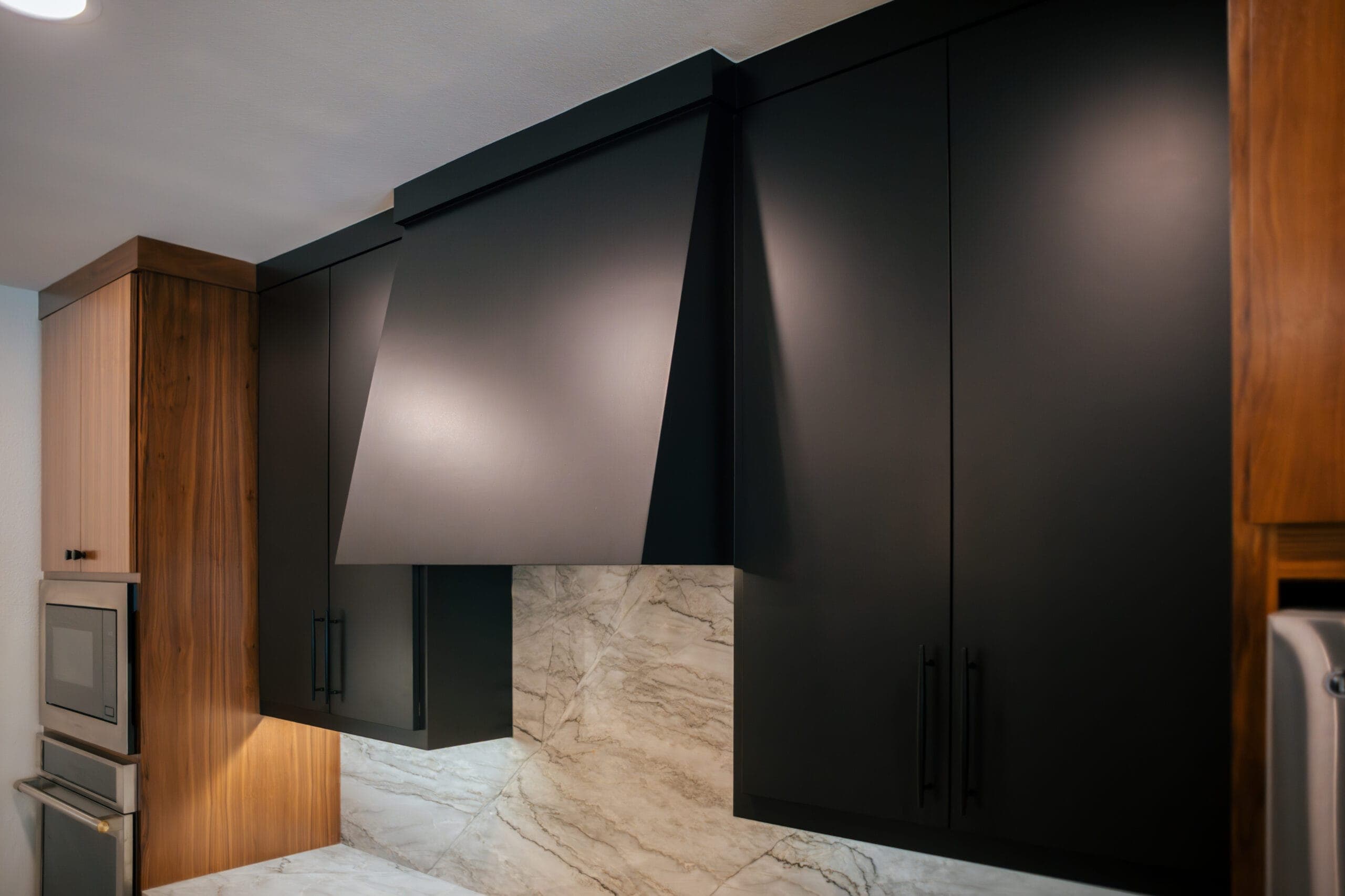 Angular matte black range hood against a full-height stone backsplash