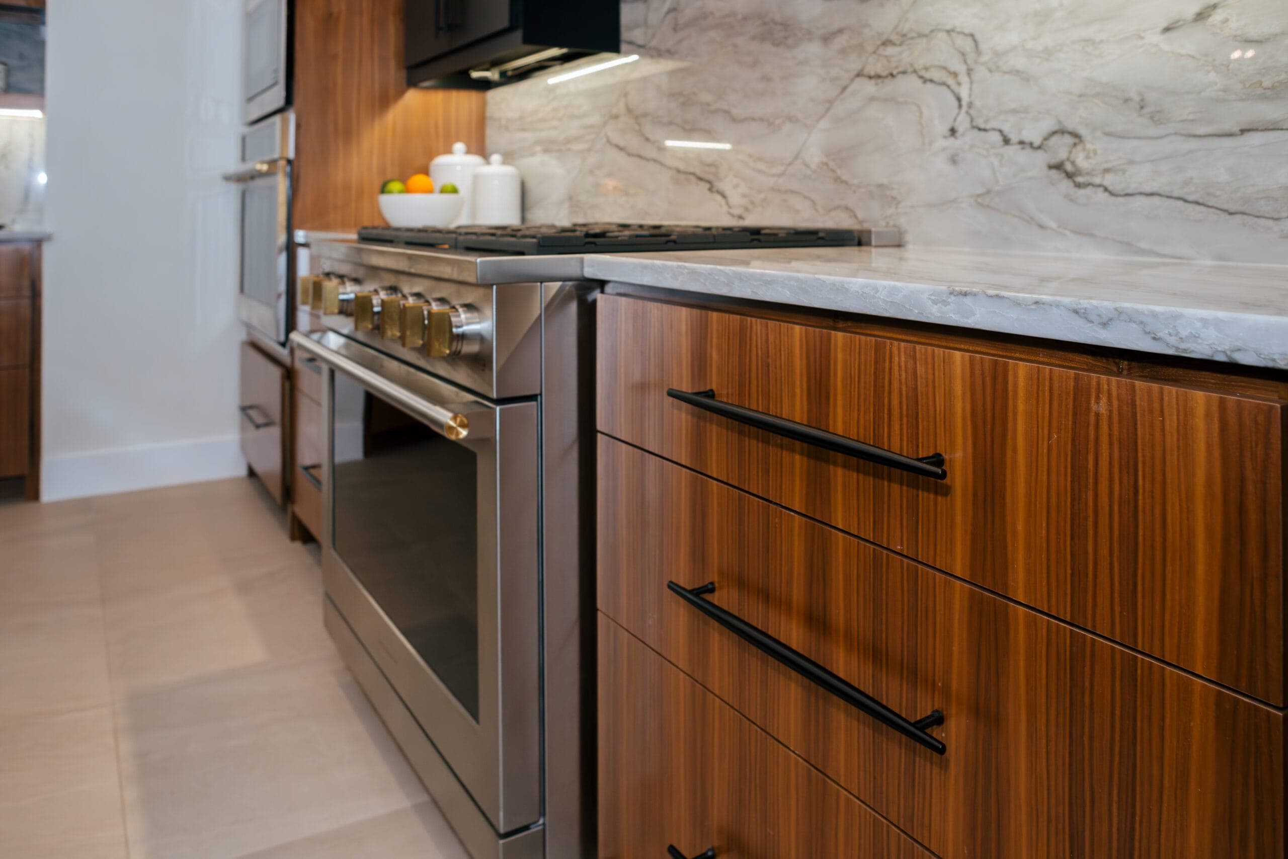 Stainless gas range flanked by walnut drawer banks and a veined stone backsplash