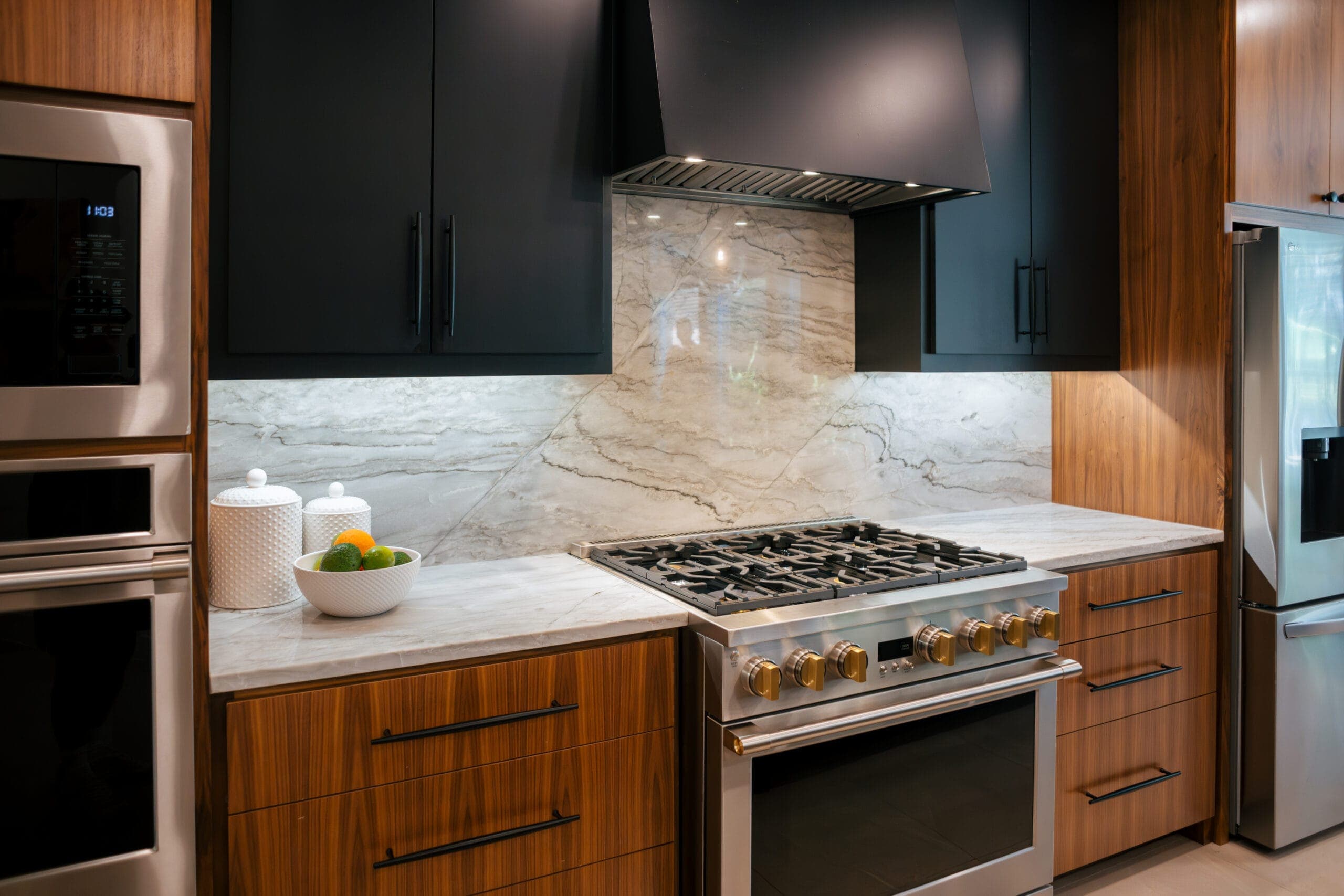 Stainless pro gas range set into walnut cabinetry under a full-height veined stone backsplash