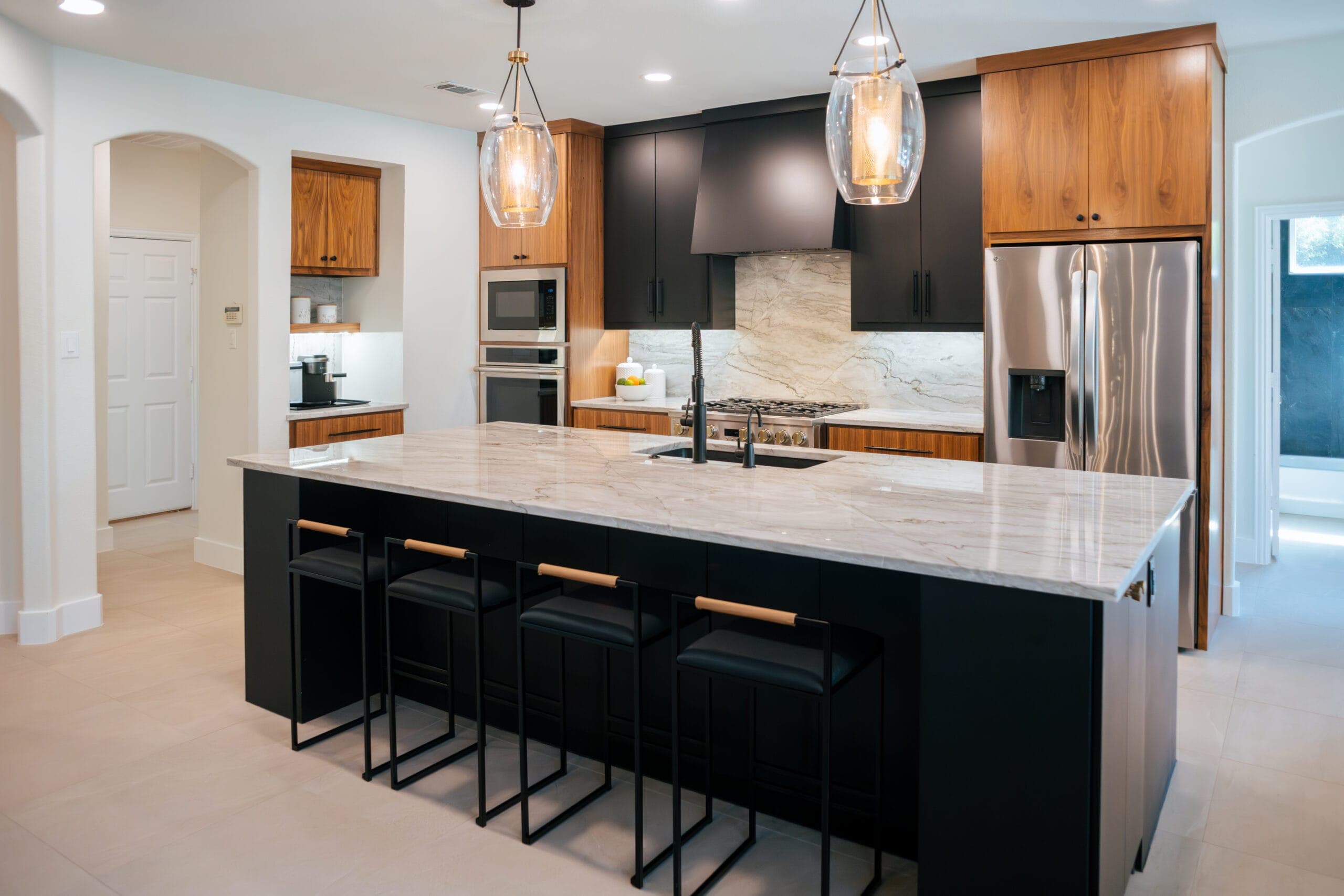Black island with four counter stools and glass lantern pendants in an open-plan kitchen — Southlake Luxury Kitchens, serving Southlake, TX