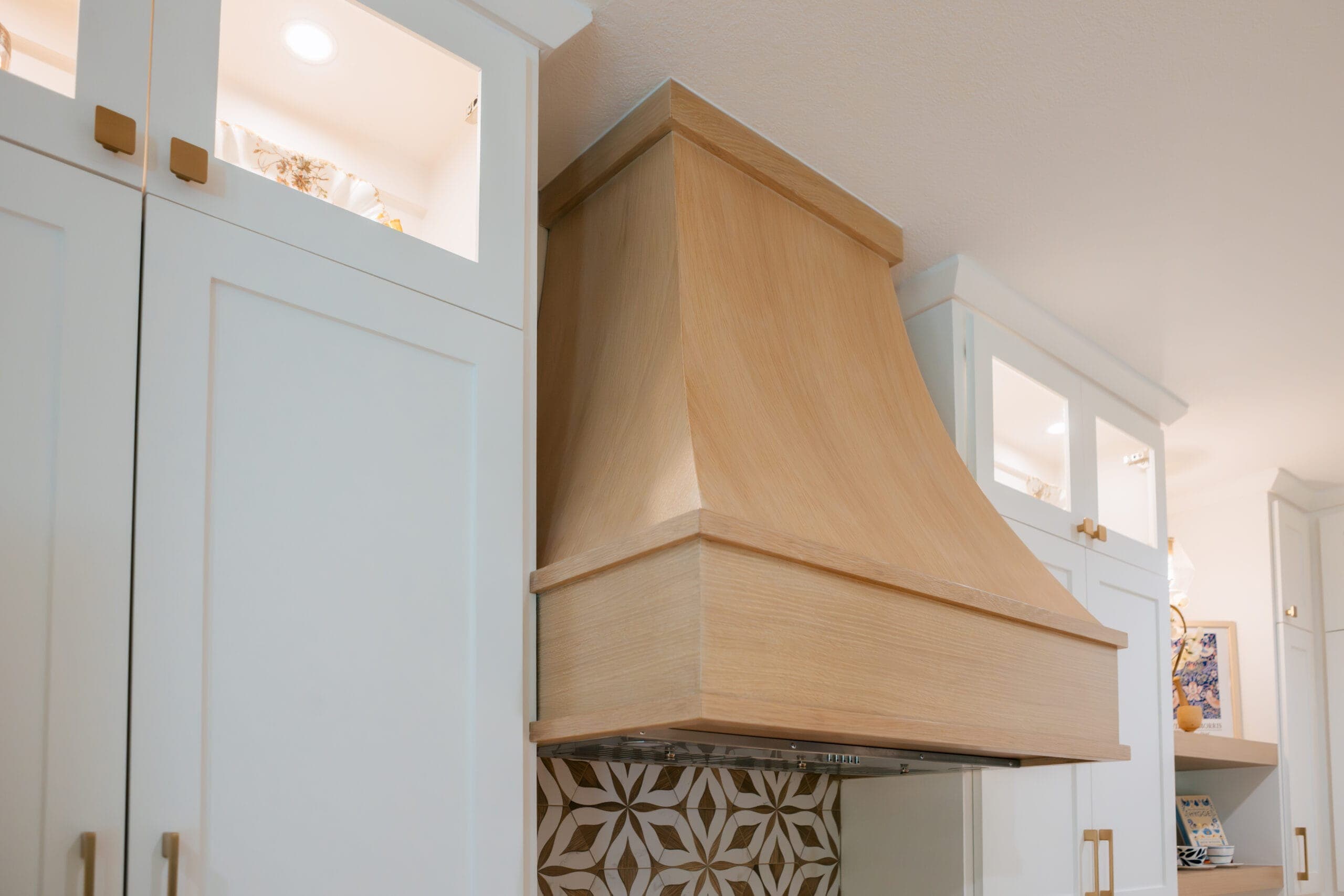 Detail of a tapered white oak range hood surround against white cabinetry