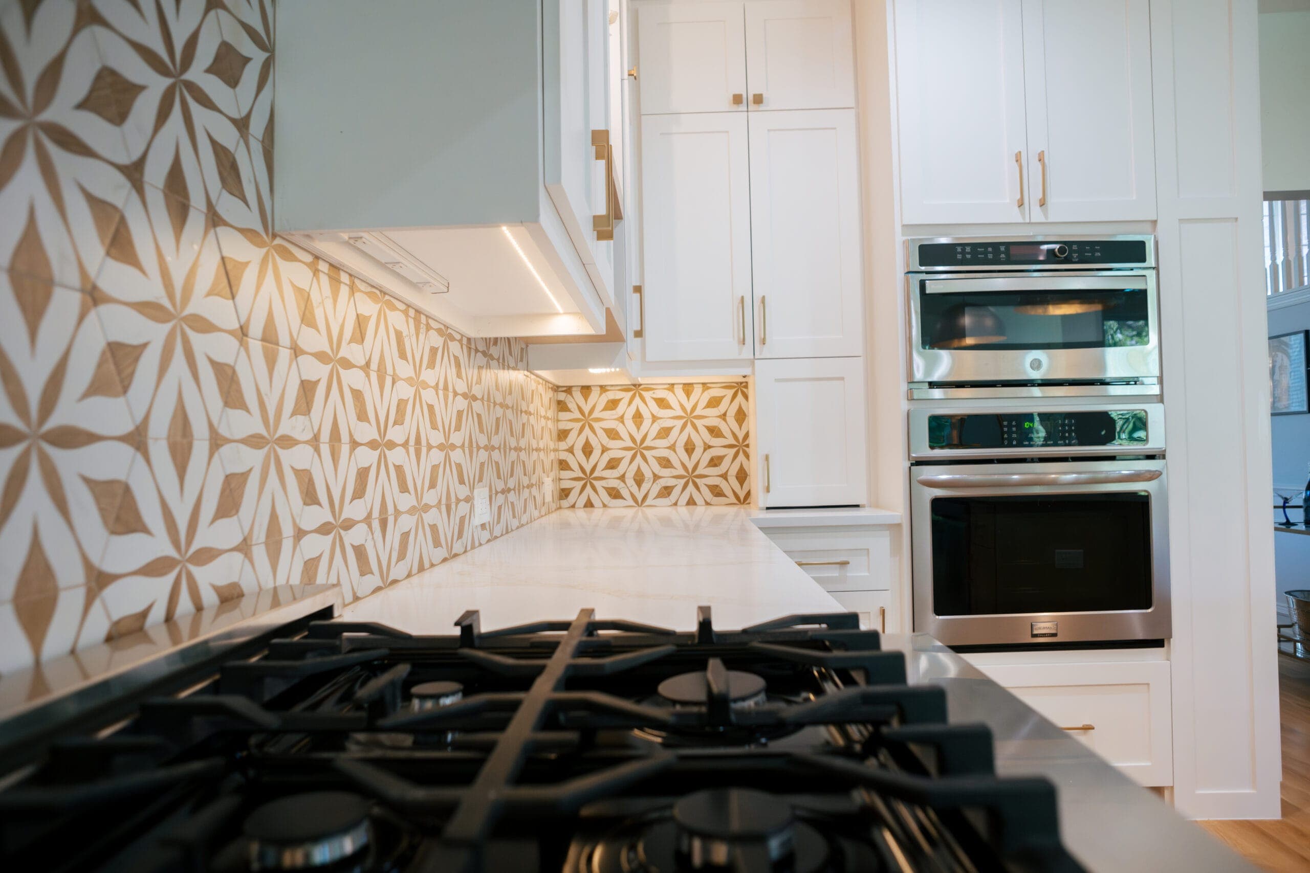 Gas rangetop burners with stainless double wall ovens and patterned tile beyond