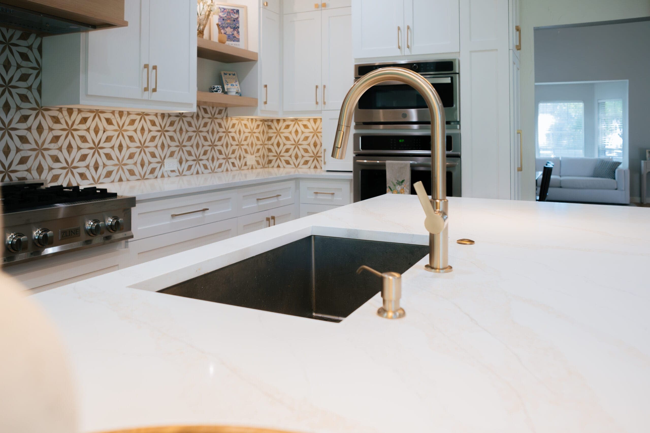 Island prep sink and brass faucet on a thick quartz counter, rangetop wall behind