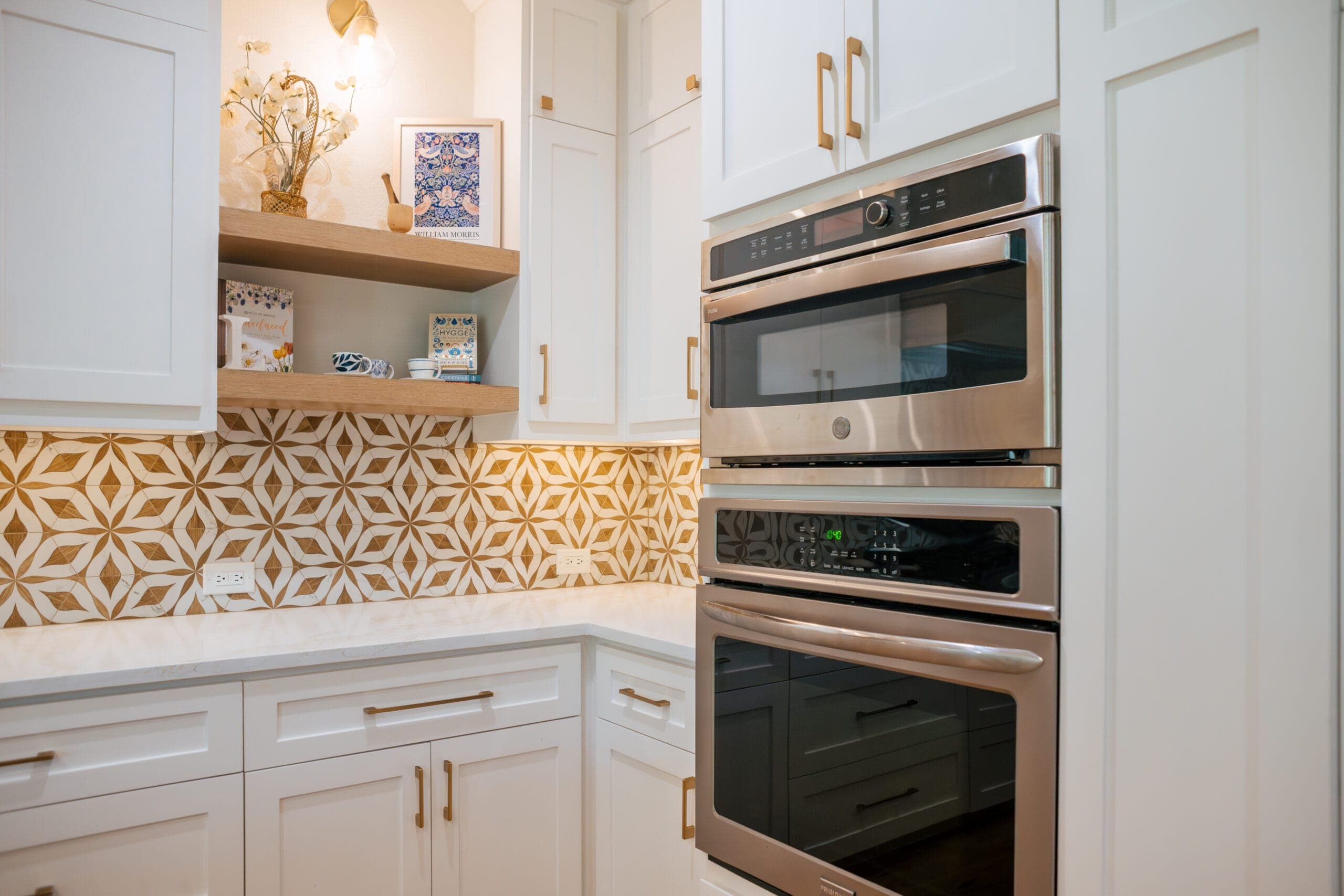 Open white oak shelving beside stainless double wall ovens in the corner of a remodeled kitchen