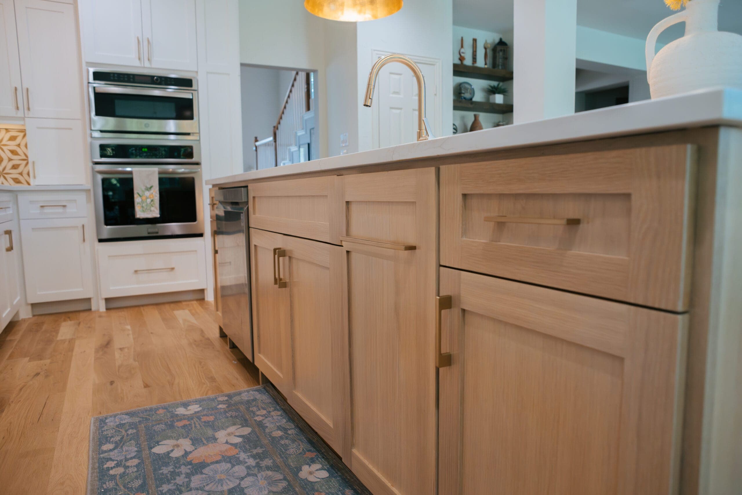 White oak cabinetry run with built-in wall ovens and a patterned runner underfoot