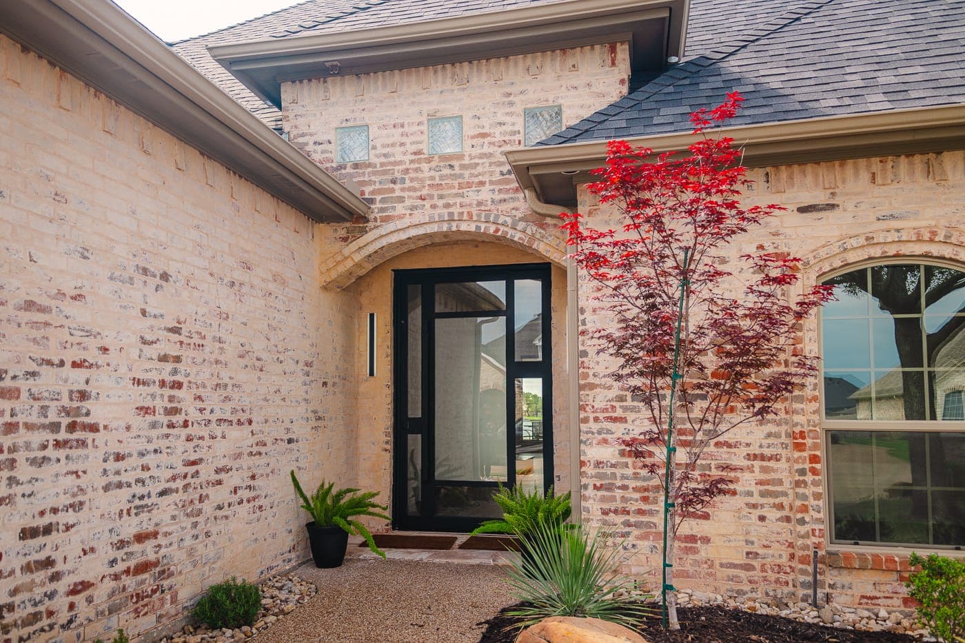 Brick entry with a black steel-and-glass front door and Japanese maple — whole-home remodeling by Southlake Luxury Kitchens, serving Southlake, TX