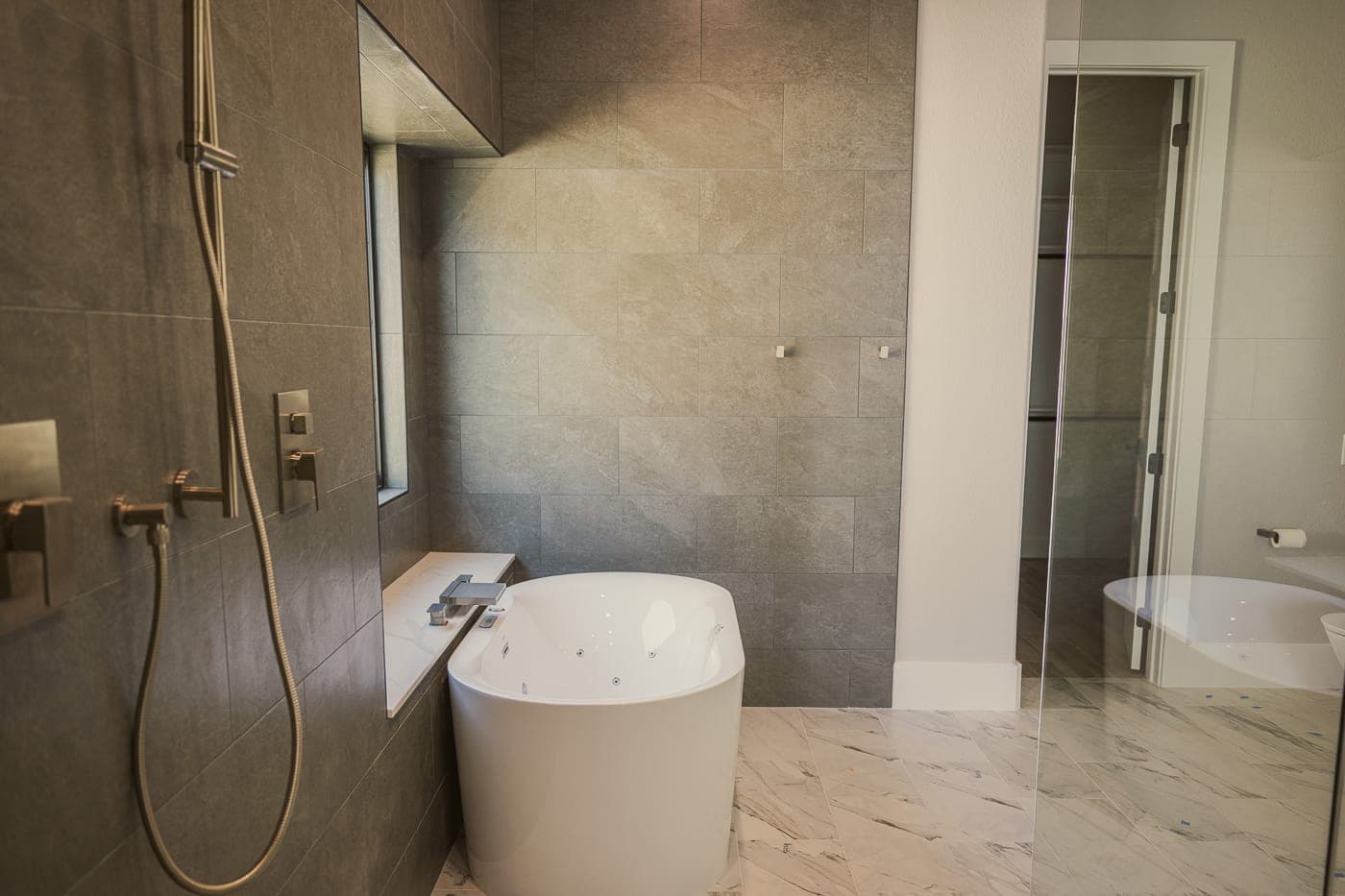 Freestanding soaking tub against large-format grey tile with brass shower fittings