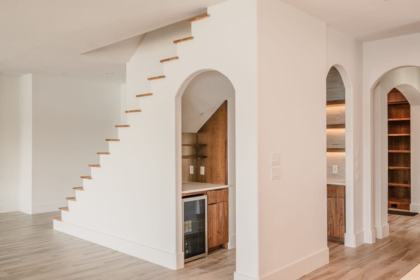 White staircase and arched openings beside a built-in wet bar