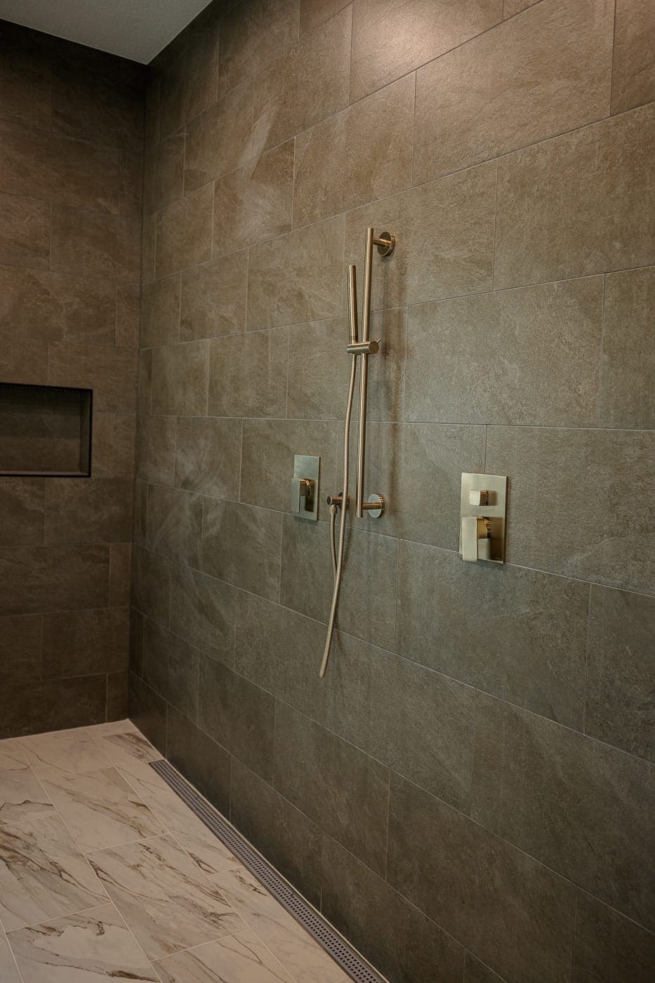 Walk-in shower finished in large-format grey tile with a recessed niche