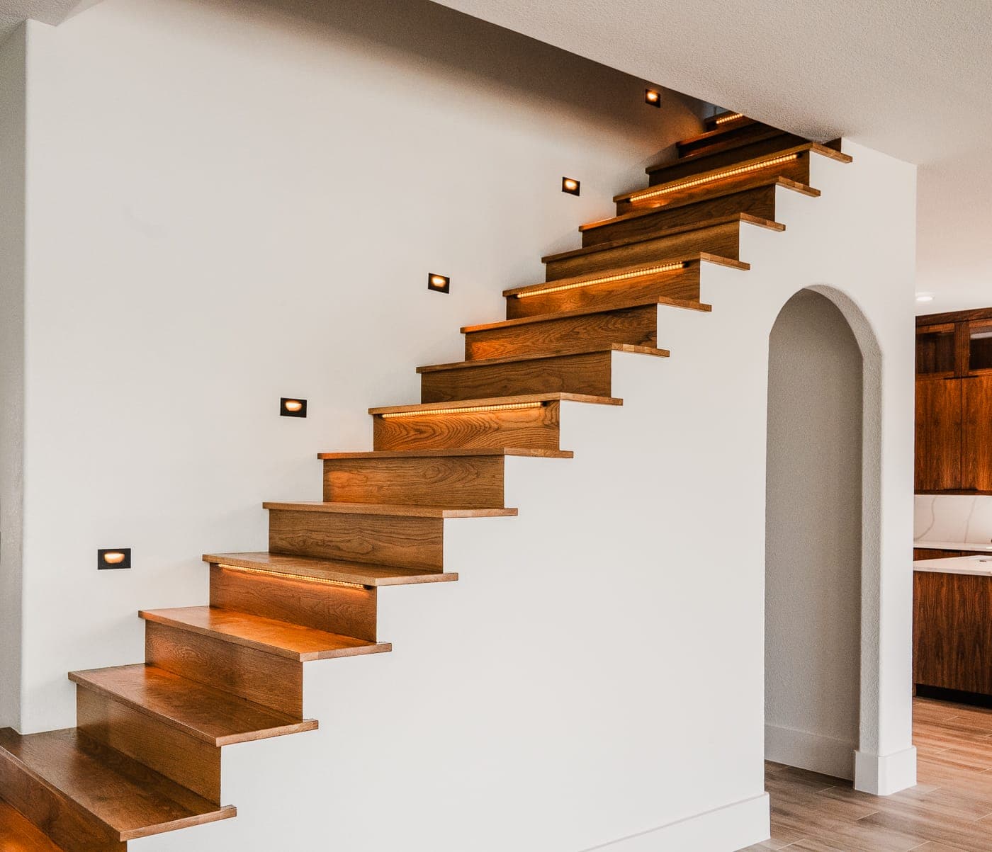 Wood staircase with lit risers against white walls
